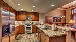 A modern kitchen with wooden cabinets, stainless steel appliances, granite countertops, and a central island with a sink. - Catamount Lodge 103 Two Bedroom (Truckee)