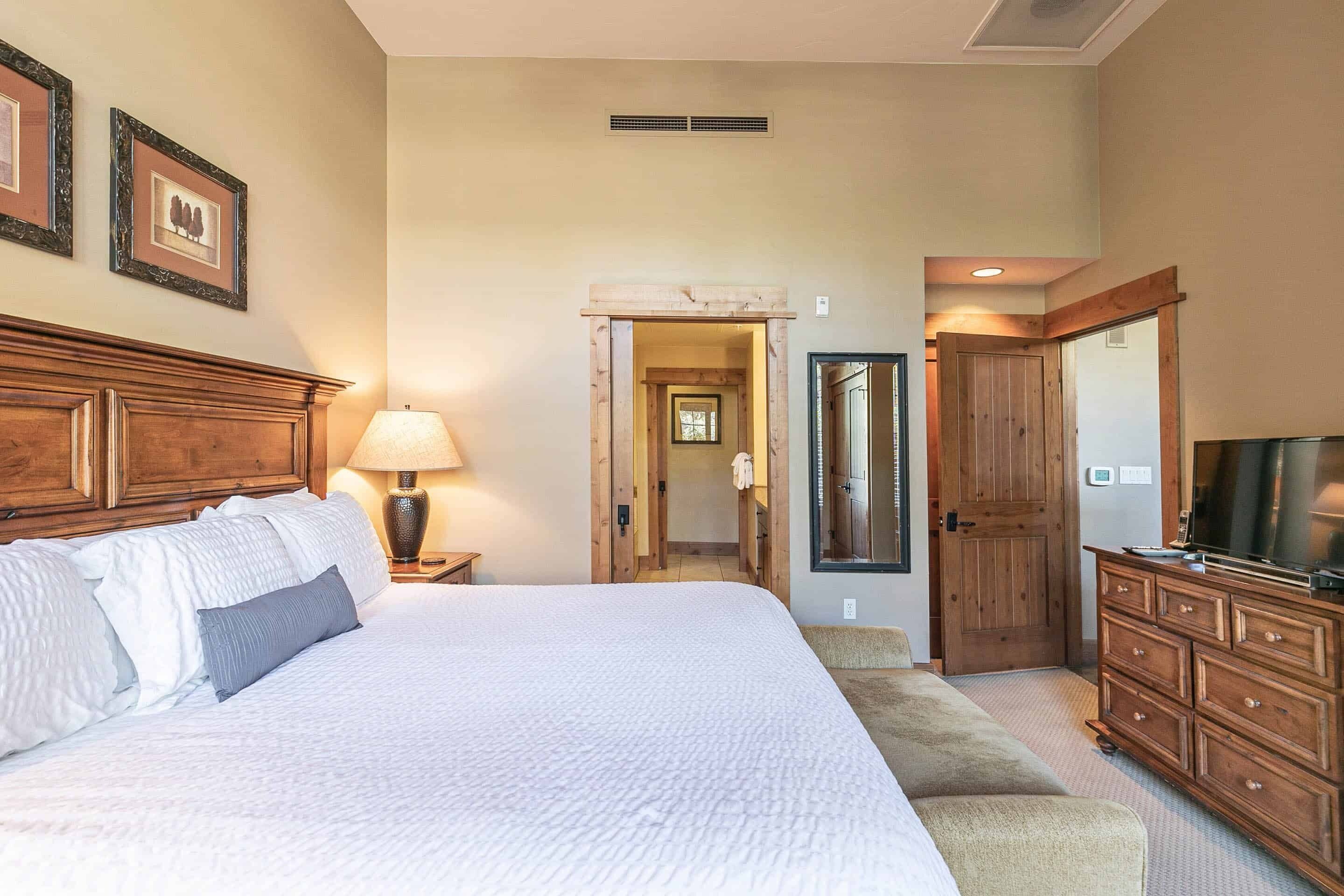 A hotel room with a large bed, wooden headboard, a television, a dresser, and a mirror.