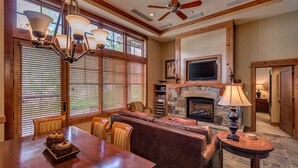 A spacious living area with a fireplace, wooden furniture, and a television mounted above it. - Catamount Lodge 103 Two Bedroom (Truckee)