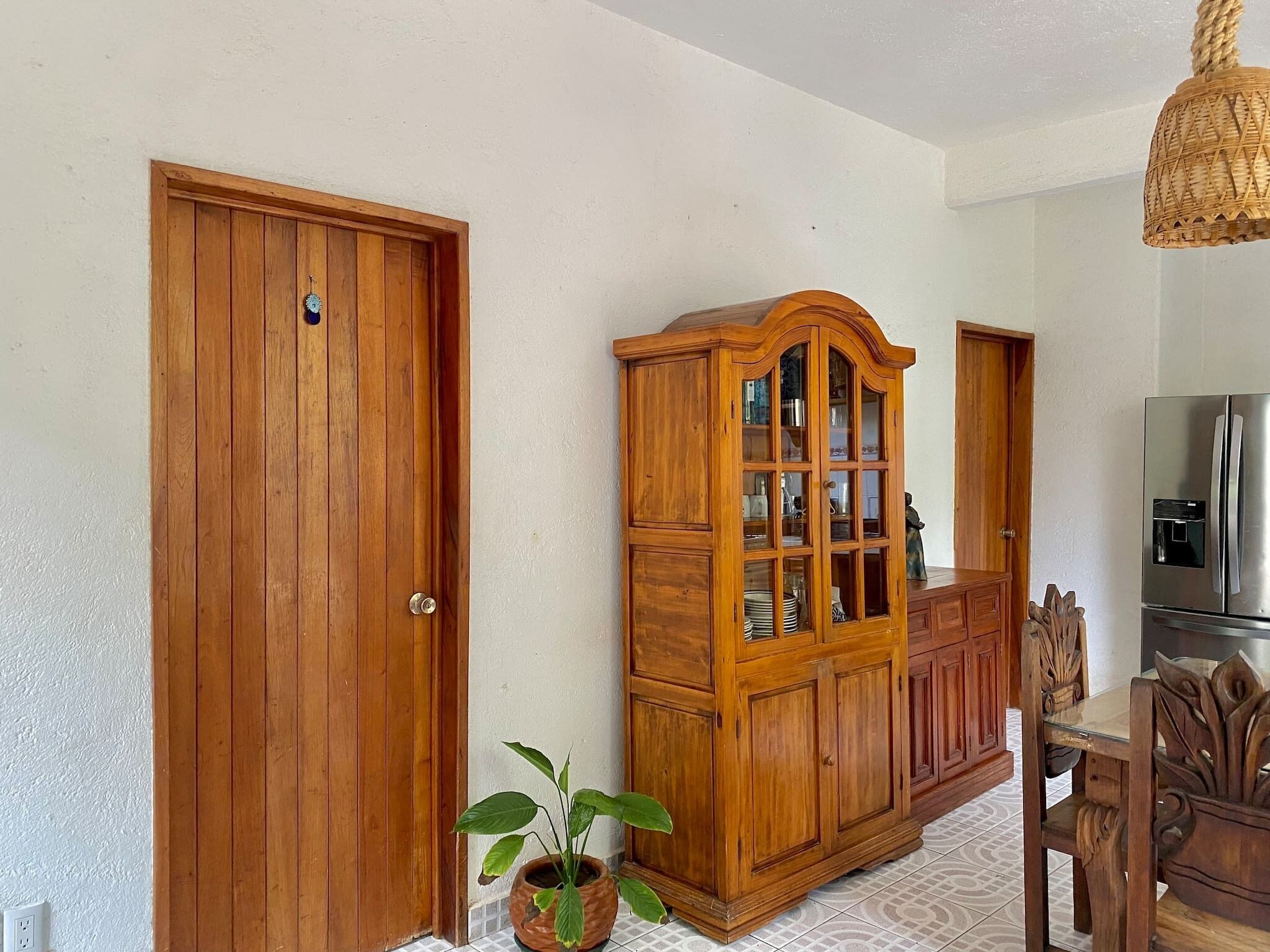 A wooden door, a wooden cabinet with glass doors, a potted plant, and a dining table with chairs.