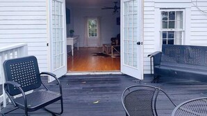 Un espace extérieur abrité, doté d’une terrasse en bois, de deux chaises en métal noir et d’un banc.