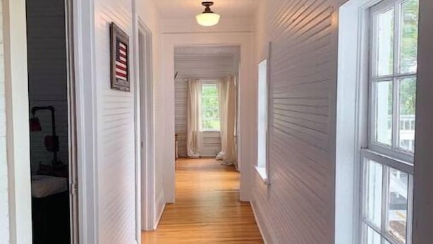 Un couloir étroit, doté de planchers en bois et de murs blancs, qui mène à une pièce avec une fenêtre.