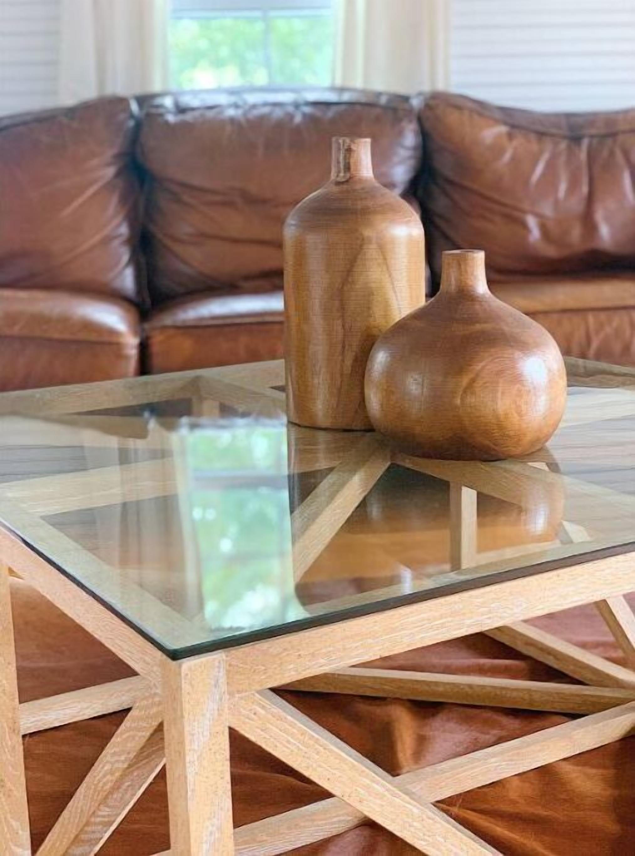 Une table à plateau en verre, sur laquelle sont posés deux vases en bois, est placée devant un canapé en cuir marron.