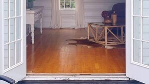 Une pièce dotée d’un plancher en bois, d’une fenêtre avec des rideaux, d’un ventilateur de plafond et d’une petite table agrémentée d’objets décoratifs.