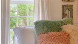 Une chambre avec une grande fenêtre, des rideaux blancs et un lit agrémenté d’oreillers moelleux.