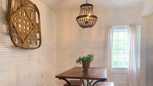 Un coin repas avec une table et des bancs en bois, un luminaire suspendu et une fenêtre avec des rideaux.