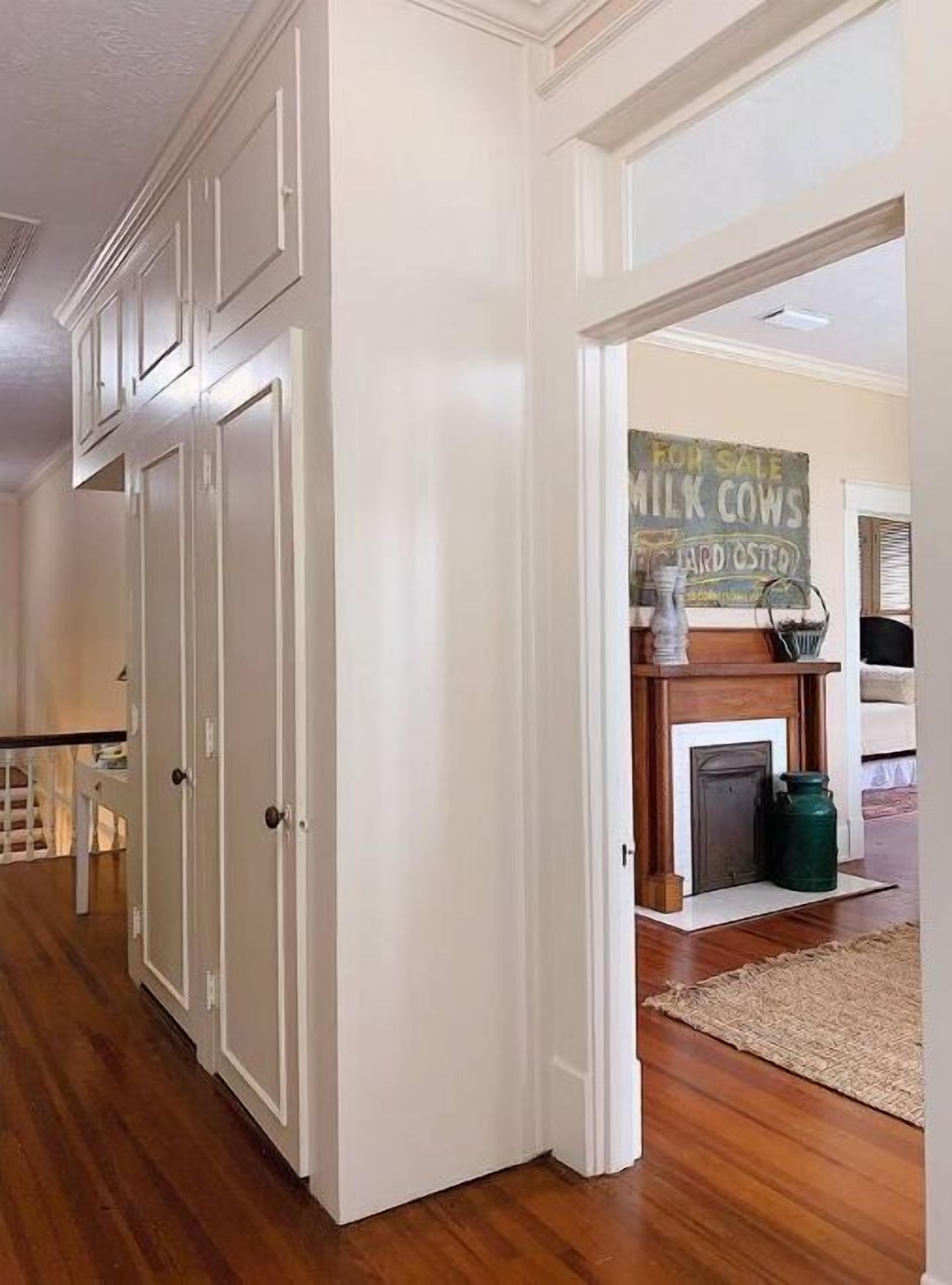 Un couloir avec des portes blanches, une cheminée sur laquelle est posée une pancarte « À vendre », et un conteneur vert sur le sol.
