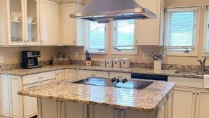 A kitchen with a central island, white cabinetry, and a stainless steel range hood. - Millarden Farms Main House (Woodbury)