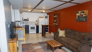 Un espacio habitable pequeño con kitchenette, un sofá marrón, una mesa de centro de madera y una alfombra estampada.