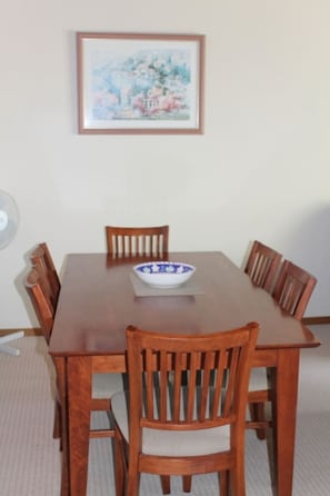A dining table with six wooden chairs, a bowl, and a framed picture on the wall.