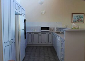 A compact kitchen with white cabinets, a microwave, and a clock on the wall.
