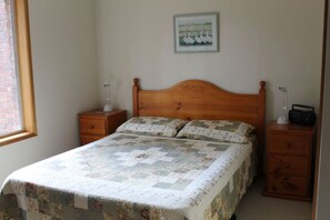 A bedroom with a wooden bed, two bedside tables, a nightstand, a framed picture on the wall, and a window.