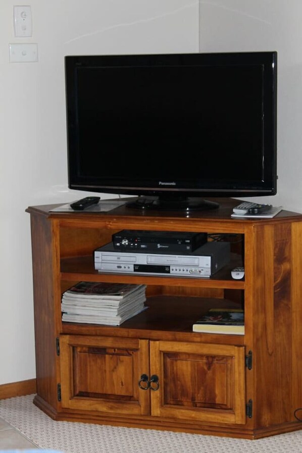 Un mueble de entretenimiento de madera con un televisor de pantalla plana, un reproductor de DVD y una pila de discos DVD.