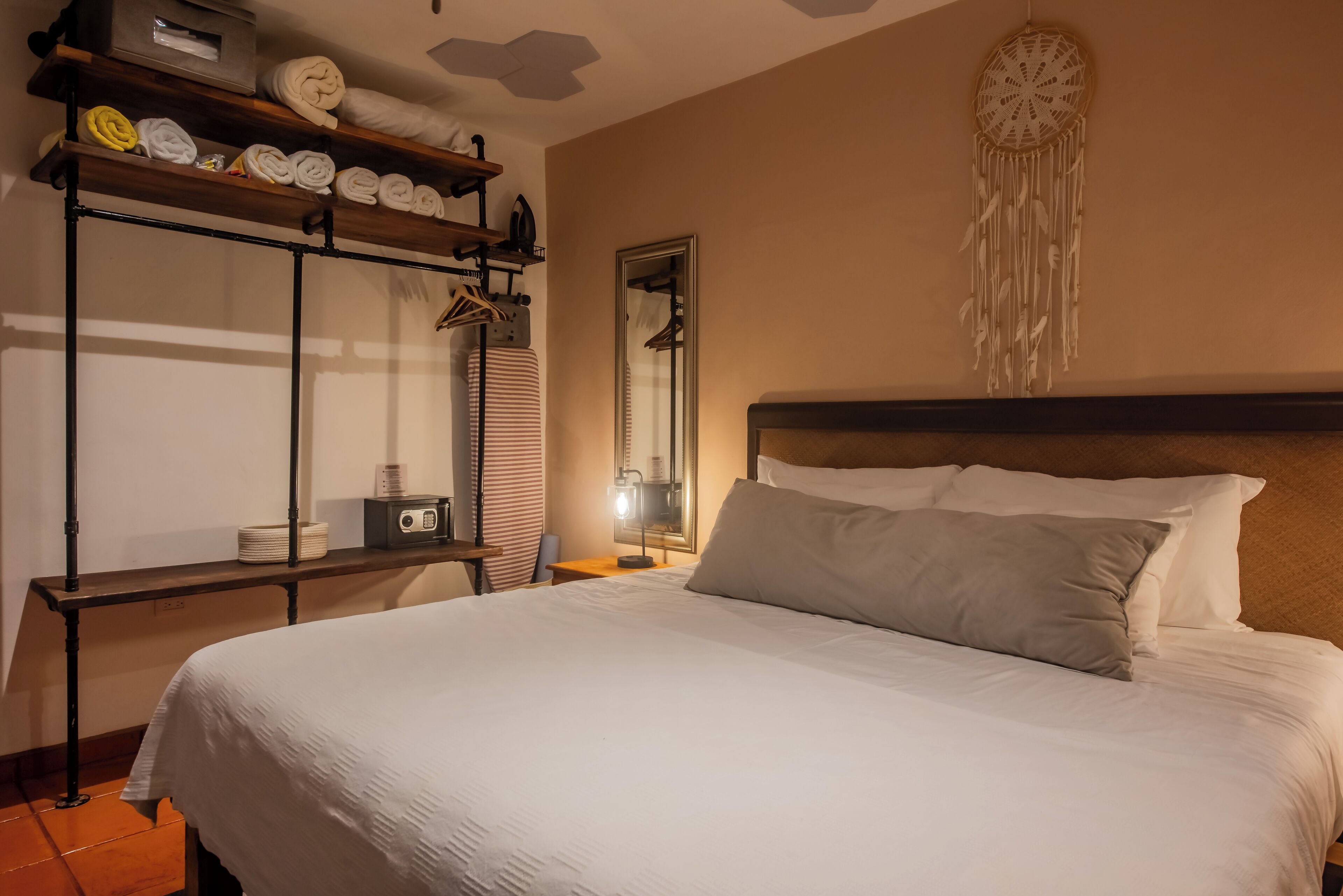 A neatly made bed with white linens, a bedside table with a lamp, and a shelf with folded towels and a radio.