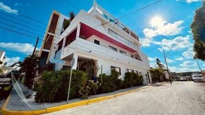 A multi-story building with a white facade and red accents, located on a street with a clear sky. - Elegant private room by a pool (Isla Mujeres)