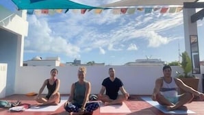 Four individuals seated on yoga mats outdoors, under a blue canopy, with a clear sky in the background. - Elegant private room by a pool (Isla Mujeres)