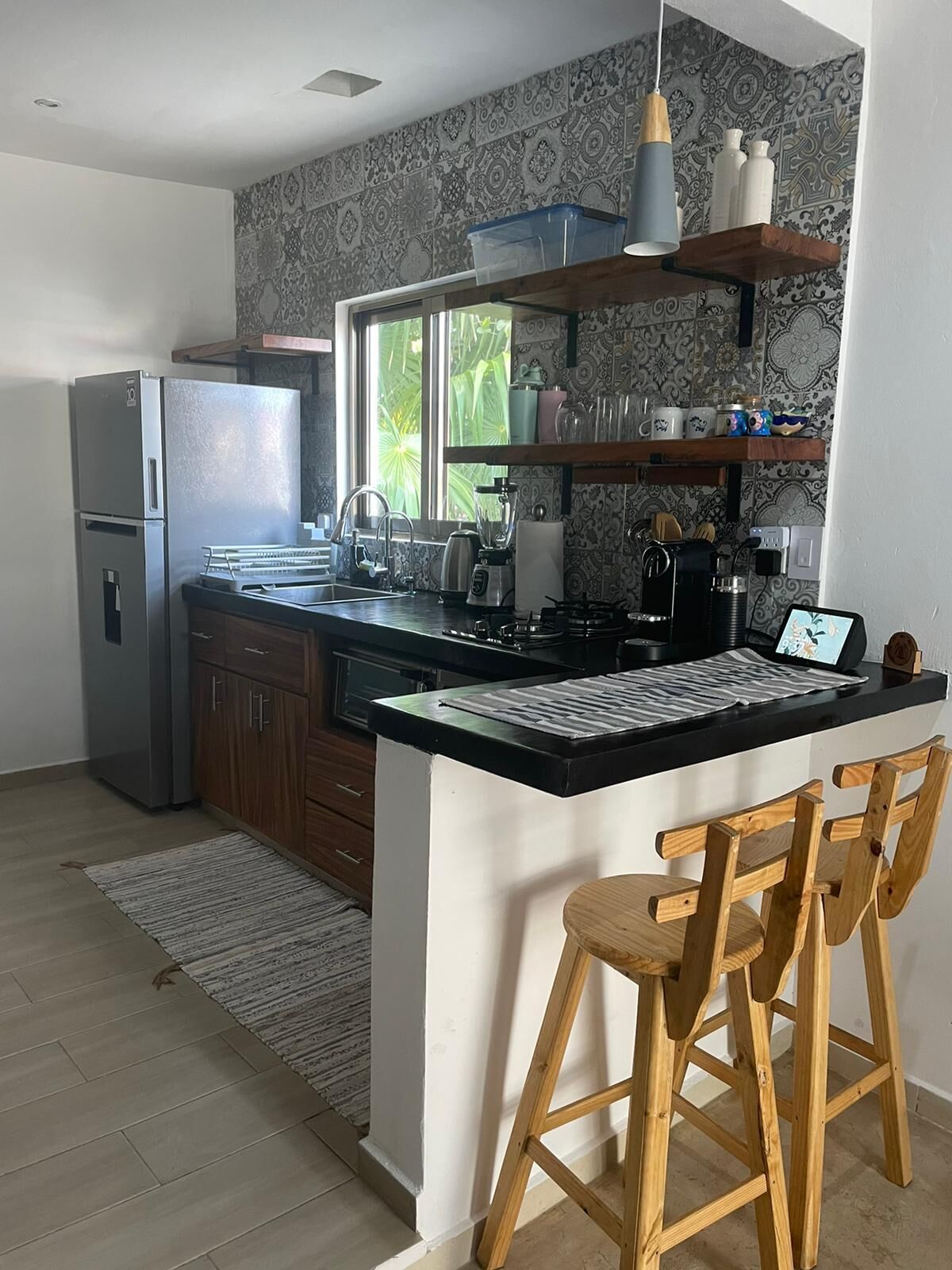 Eine moderne Küche mit einer zentralen Kochinsel, Holzbarhocker, einem Kühlschrank und Wandtapete mit Muster.