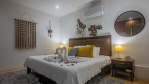 A neatly made bed with a white bedspread, two pillows, and a decorative swan made of towels. There is a nightstand with a lamp and a mirror on the wall.