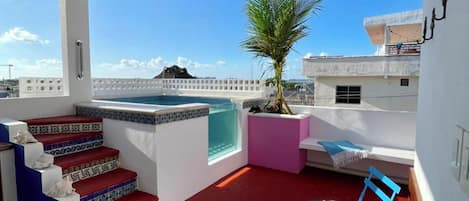 A rooftop terrace with a pool, a palm tree, and a seating area with a table and chairs.