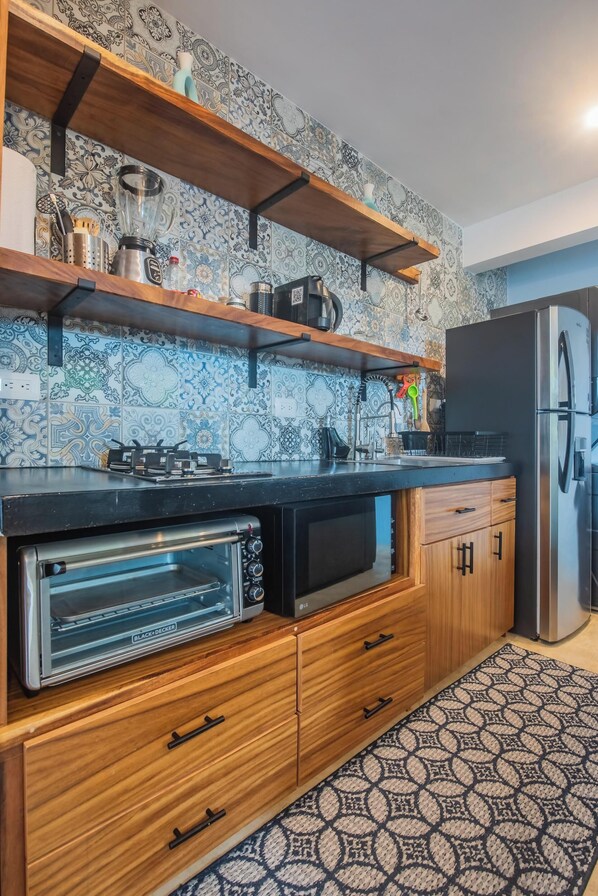 Una cocina con salpicadero decorativo, armarios de madera, horno empotrado, microondas, estufa a gas y refrigerador.
