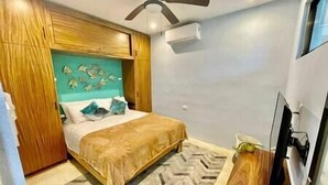Un dormitorio con cama, ventilador de techo, aire acondicionado mural y televisor.