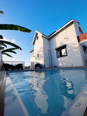Ein modernes Gebäude mit Schwimmbad, einer Holzterrasse und einer weißen Fassade.
