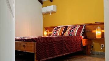 Une chambre avec un lit en bois, un mur jaune et un plafond en pente avec des poutres en bois.