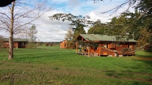 Una cabaña rústica con porche, rodeada por un campo cubierto de hierba y árboles.