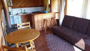 Cocina compacta con gabinetes de madera, una barra con taburetes, una mesa de comedor con sillas y un sofá.