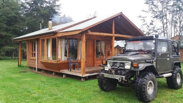 Una cabaña de madera con un porche y una camioneta SUV grande estacionada frente.