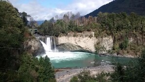 Una cascada vertiginosa que desemboca en un río, rodeado de un bosque frondoso y montañas.
