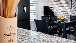 Una cocina moderna con encimera de granito, un portalapiedras de madera, un refrigerador negro y una zona de comedor con mesa y sillas.
