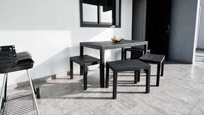 Un comedor moderno con una mesa rectangular y cuatro sillas, una parrilla pequeña a la izquierda y una ventana sobre la mesa.