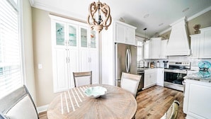 A kitchen with white cabinets, a stainless steel refrigerator, an oven, and a dining table with chairs.