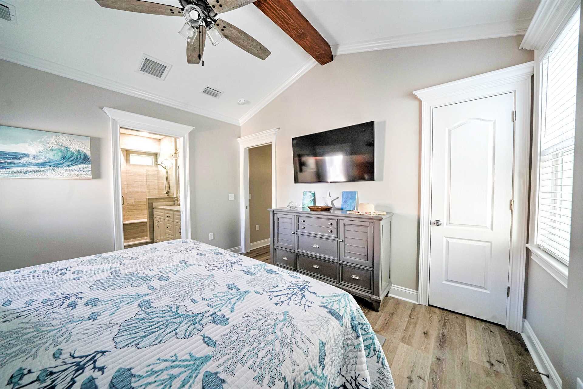 Une chambre à coucher avec un lit, une commode, un ventilateur de plafond, une porte et un tableau accroché au mur.