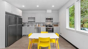 A modern kitchen with white cabinets, stainless steel appliances, and a bright yellow dining table. - Luke's Jedi Meditation Chamber (Seattle)