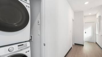 A laundry room with stacked washers and dryers, a white wall, and a wooden floor.