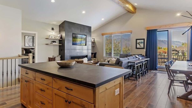 A spacious kitchen with a large island, a dining area with a long table, and a living room with a sofa and a fireplace. - Spectacular Mountain Oasis (Eden)