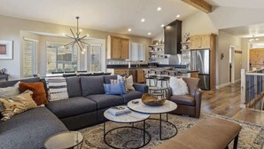 A spacious living area with a sofa, coffee table, and ottoman, a kitchen with wooden cabinets, and a dining area with a chandelier. - Spectacular Mountain Oasis (Eden)