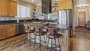 A modern kitchen with wooden cabinets, a stainless steel refrigerator, and a central island with bar stools. - Spectacular Mountain Oasis (Eden)