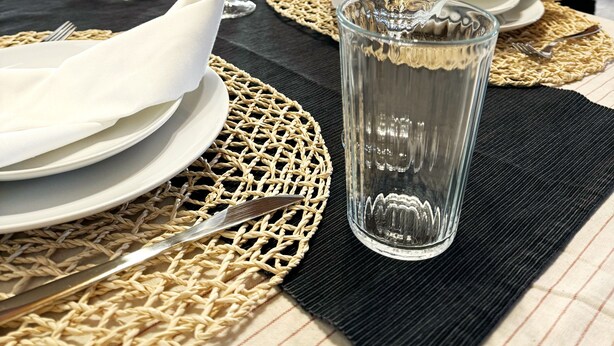 A dining table set with plates, glasses, and cutlery, with a woven placemat and a fruit bowl in the background. - House of the Apricot trees - independent house/ free parking (Spinea)
