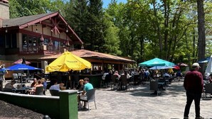 An outdoor dining area with tables and chairs, surrounded by trees and a building with a red roof. - Winter fun near Big Boulder Mountain! (Lake Harmony)