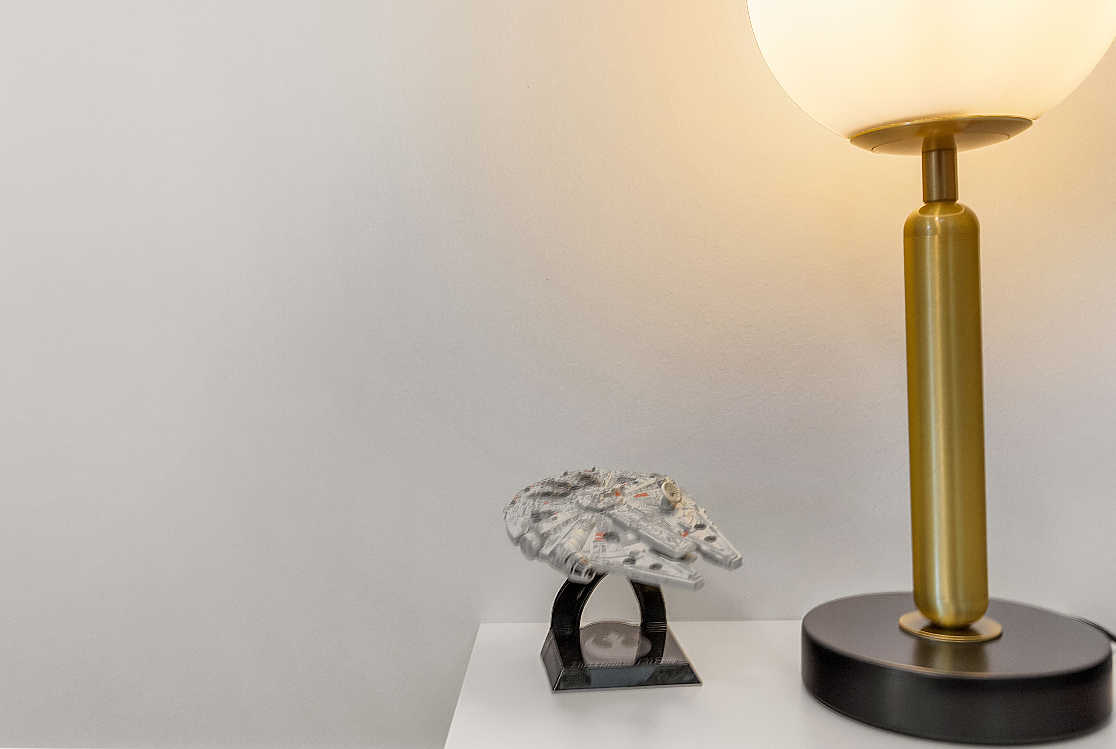 A lamp with a round shade and a metallic base, placed on a white surface next to a model of a spacecraft.