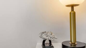 A lamp with a round shade and a metallic base, placed on a white surface next to a model of a spacecraft.
