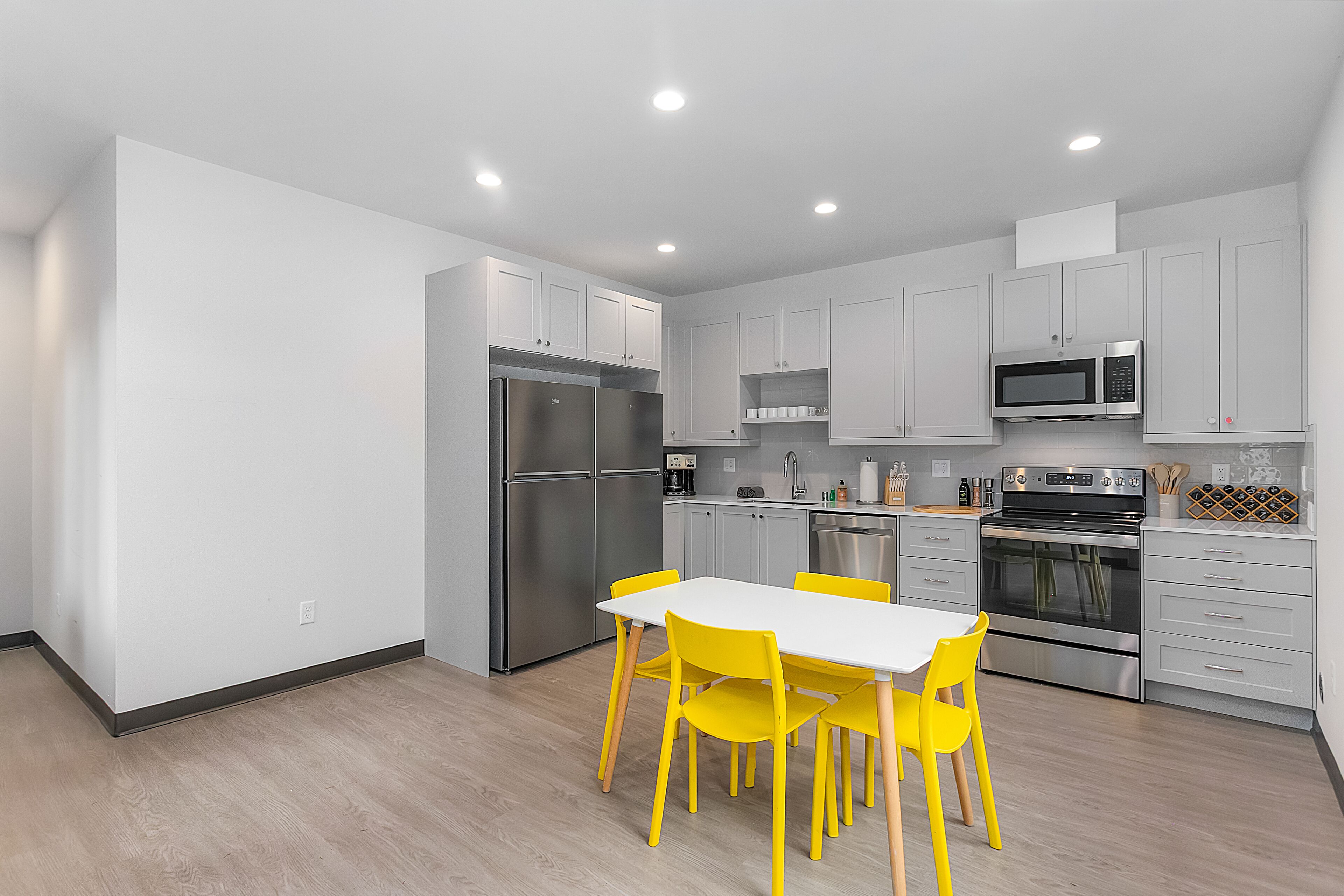 A modern kitchen with white cabinets, stainless steel appliances, and a dining area with yellow chairs.