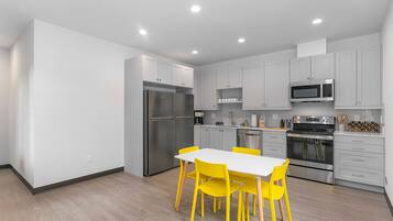 A modern kitchen with white cabinets, stainless steel appliances, and a dining area with yellow chairs.