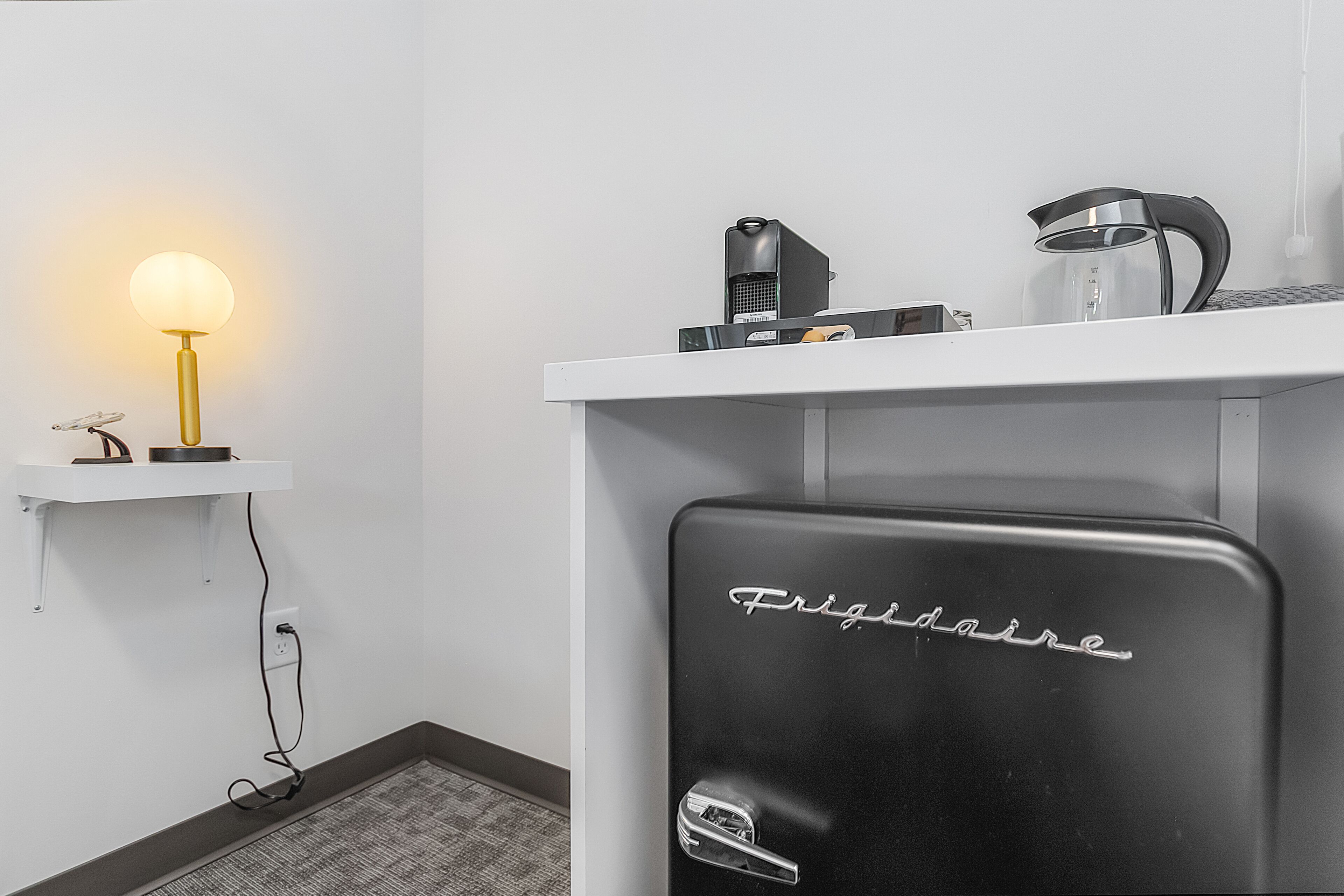A kitchen with a Frigidaire refrigerator, a coffee maker, and a lamp on a shelf.
