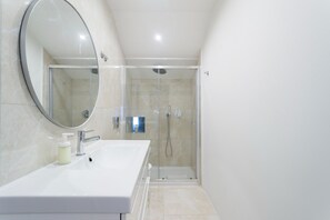 Features a large mirror, white sink, and glass-enclosed shower with handheld showerhead.