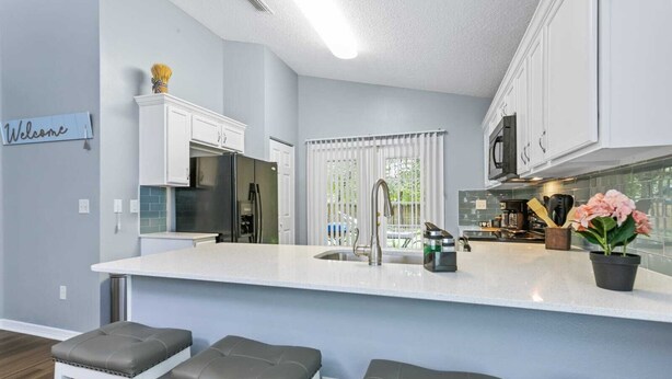 A modern kitchen with a central island, white cabinetry, and a 'Welcome' sign on the wall. - Huge backyard and new reconstruction  (St. Augustine)