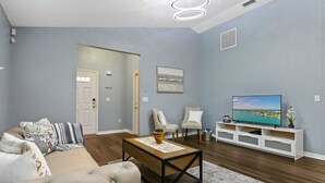 A living room with a sofa, chairs, a coffee table, and a TV on a white stand. - Huge backyard and new reconstruction  (St. Augustine)